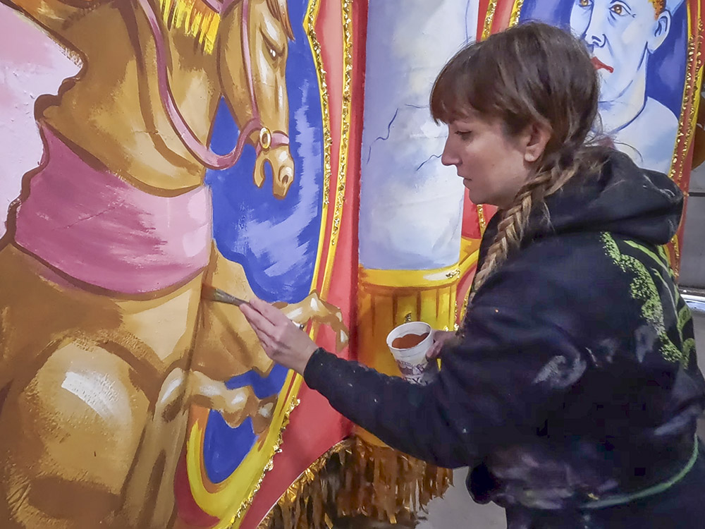 woman in dark sweatshirt painting on colorful mardi gras float