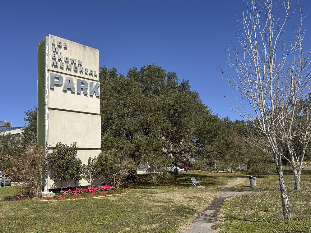 large entrance sign to Joe Brown Park under blue sky with green trees and grass