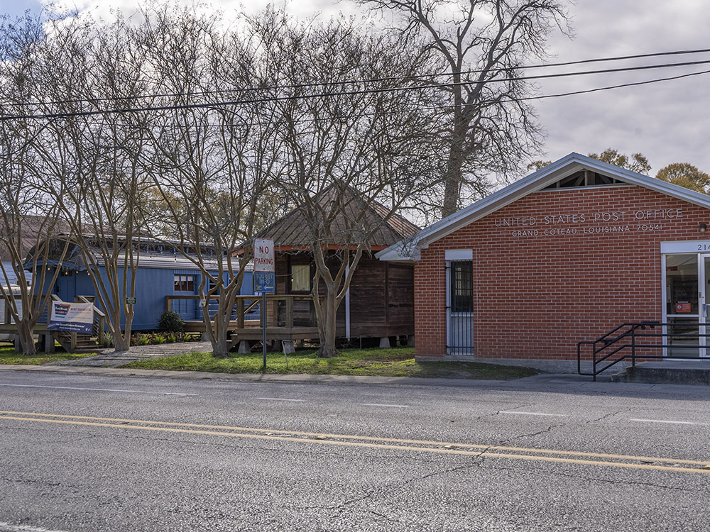 red brick post office on highway next to wood structure and blue railroad carf