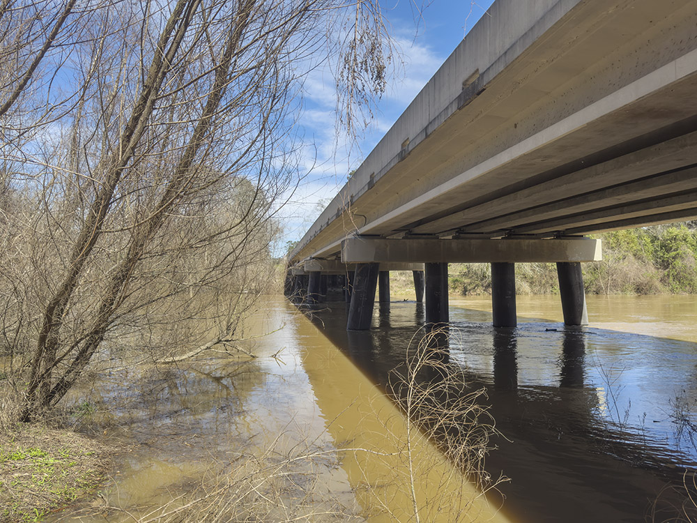 side of a bridge above waterwayk with trees along riverbank