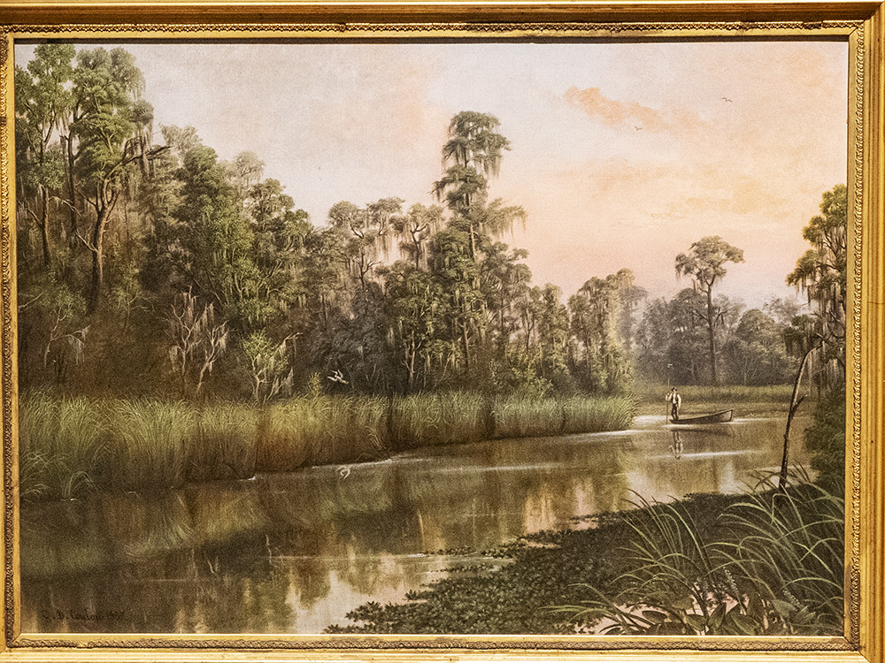 framed oil painting showing man in row boat in waterway in cypress tree forest