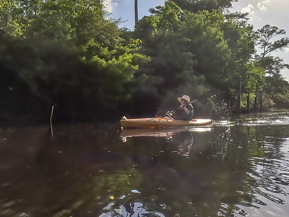 woman wearing blue shirt and straw hat paddles orange-yellow kayak