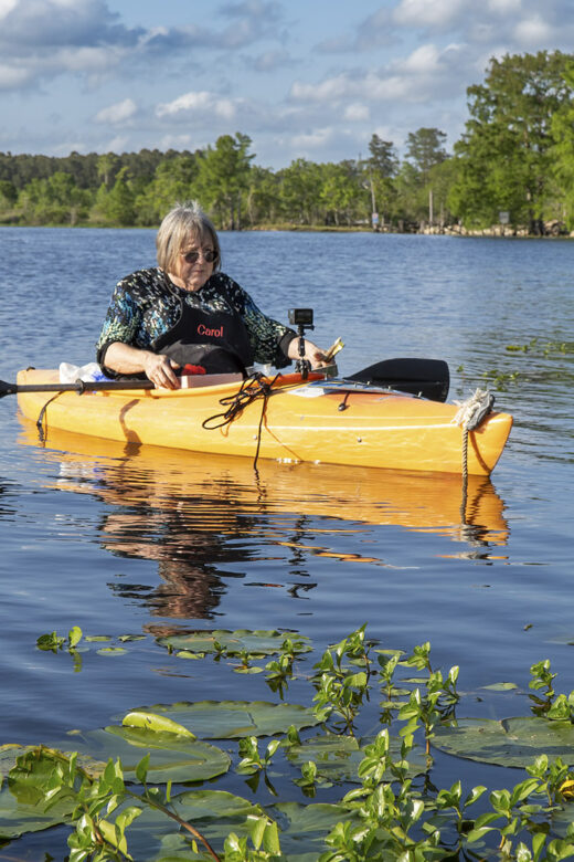woman artist in kayak along bayou with trees and blue sky