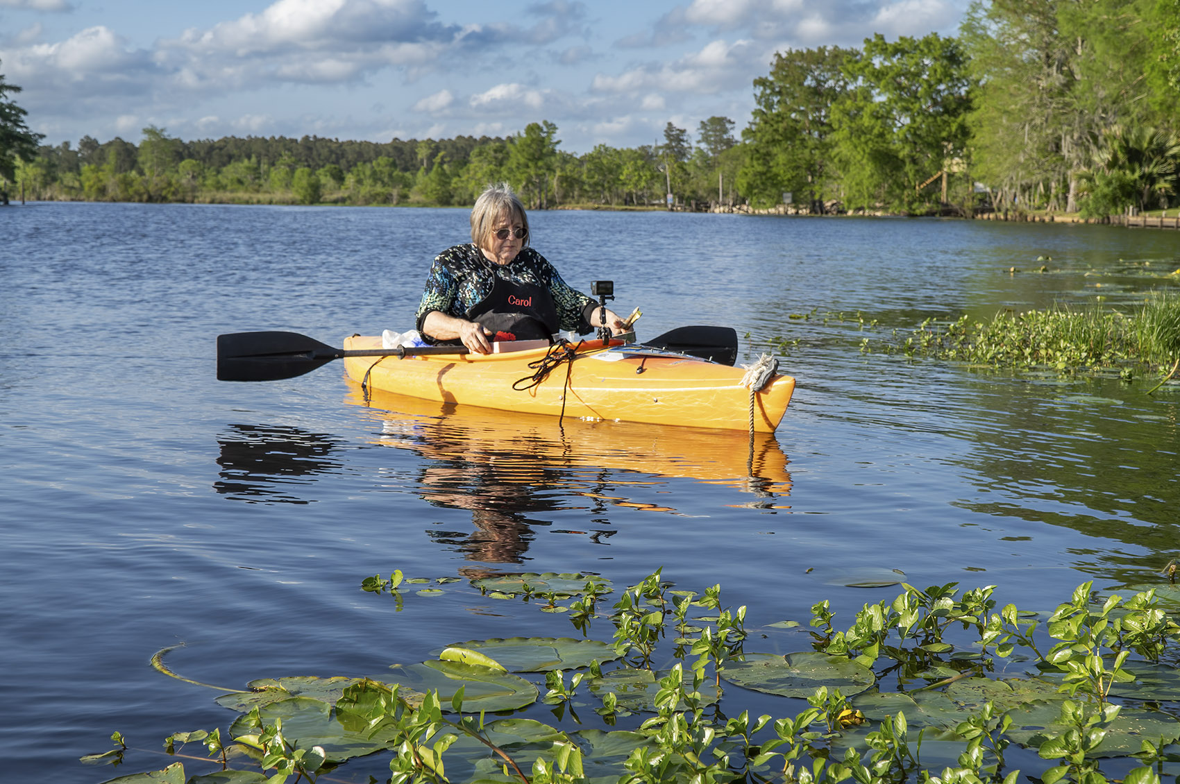 woman artist in kayak along bayou with trees and blue sky