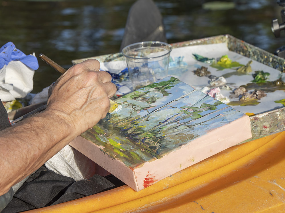 woman artist paints tree scene in kayak