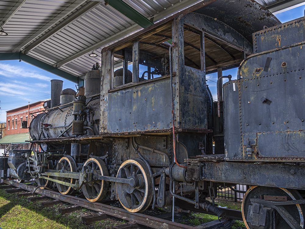 old rusting black steam locomotive on display under pavilion