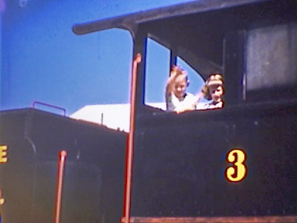 young boy and girl wave from black painted train engine number 3 in old photograph