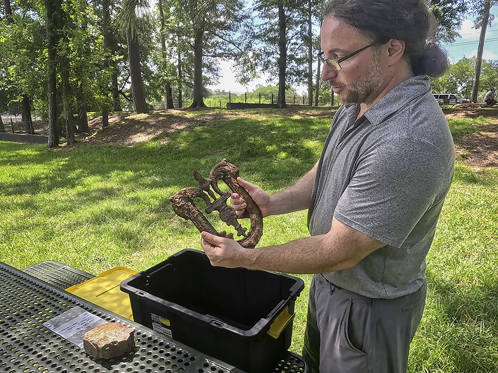 man in gray shirt and glasses holds rusted iron piece from LSU origin campus