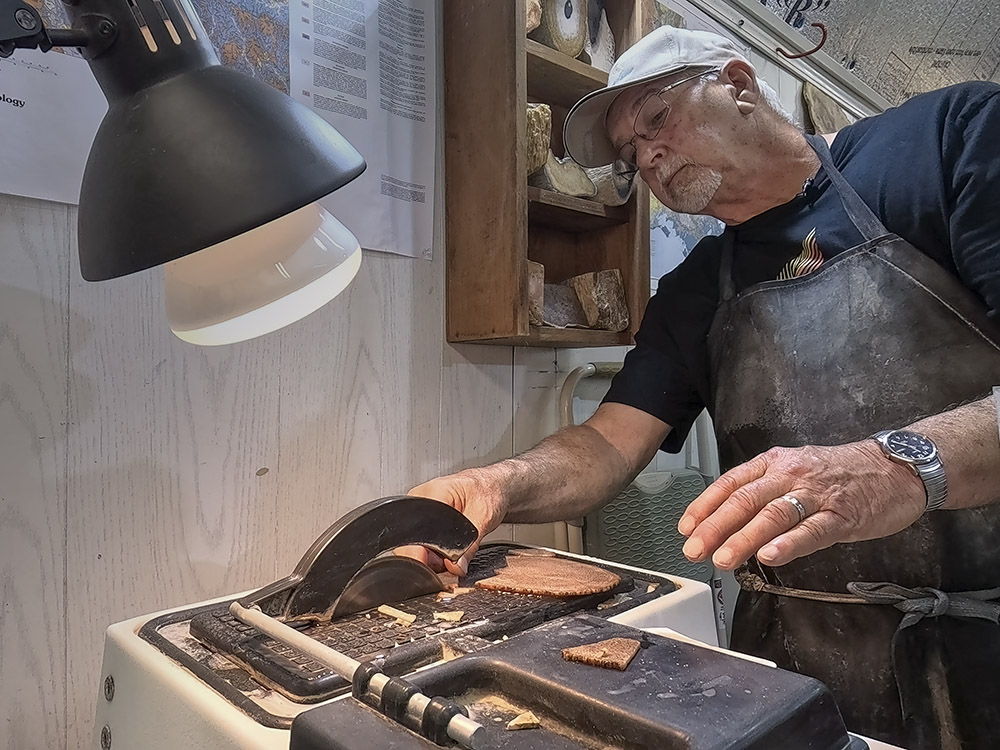 man wearing apron, dark shirt and white cap cutting pieces of stone with table saw