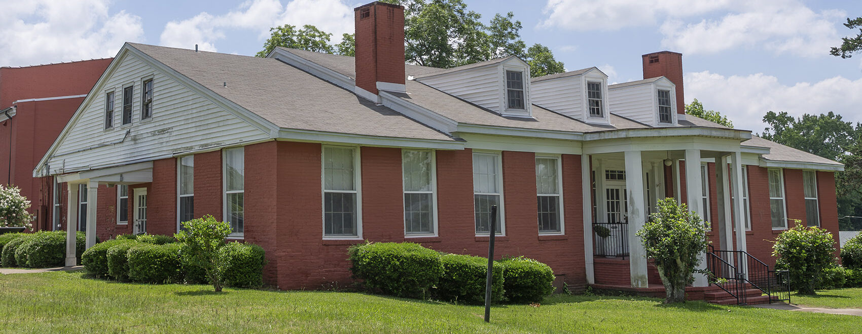 red brick one and a half story house with two chimneys and white columns at entrance