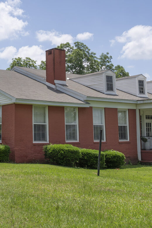 red brick one and a half story house with two chimneys and white columns at entrance
