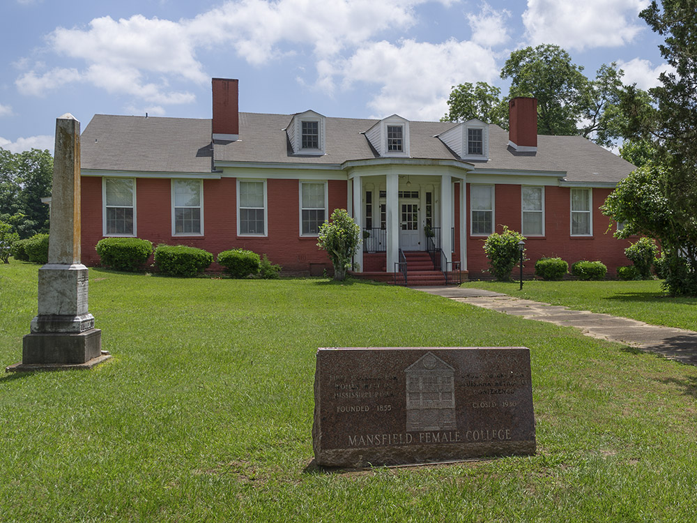 red bricks house building with white columns at front entrance and stone sign for first female college