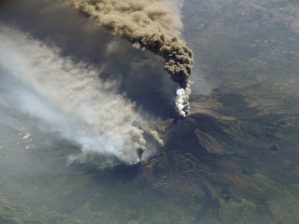 aerial view of equpting volcano and plume of smoke and ash