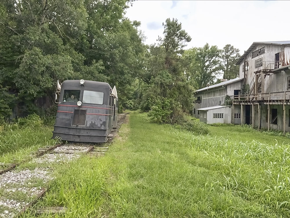 old green rail car on tracks next to sawmill