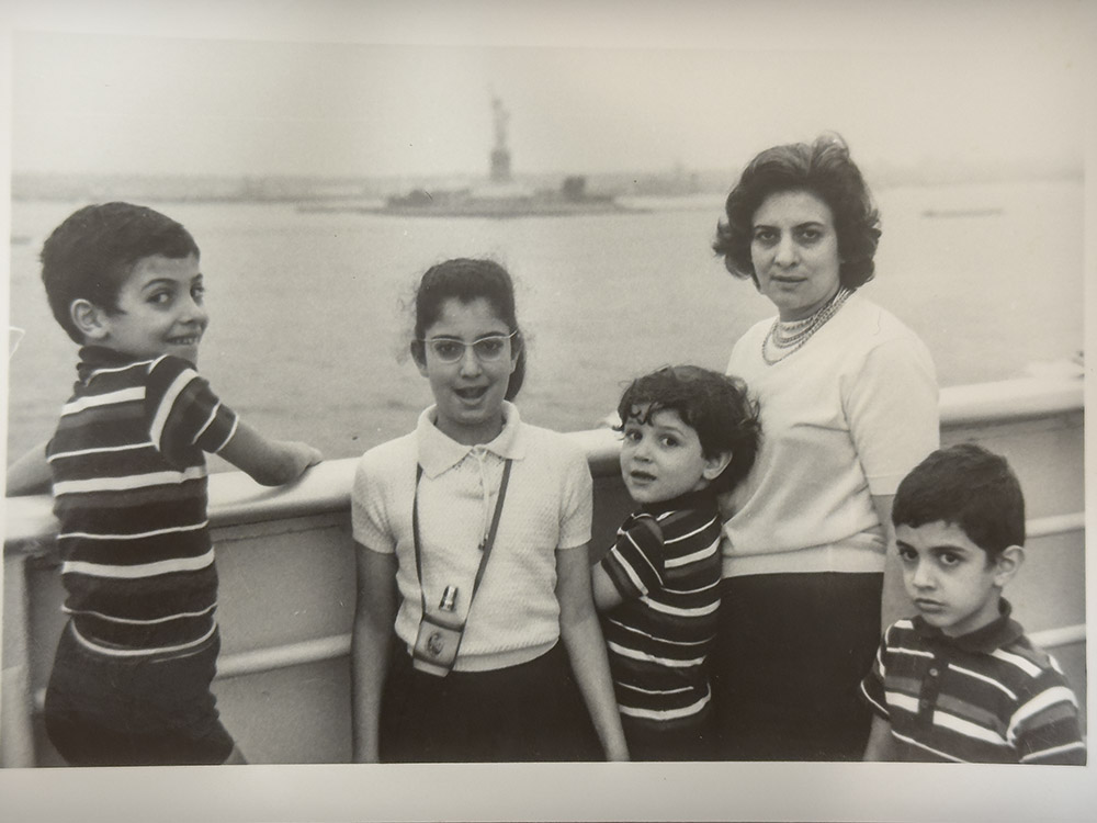 black and white image of woman and four children passing statue of liberty on ship