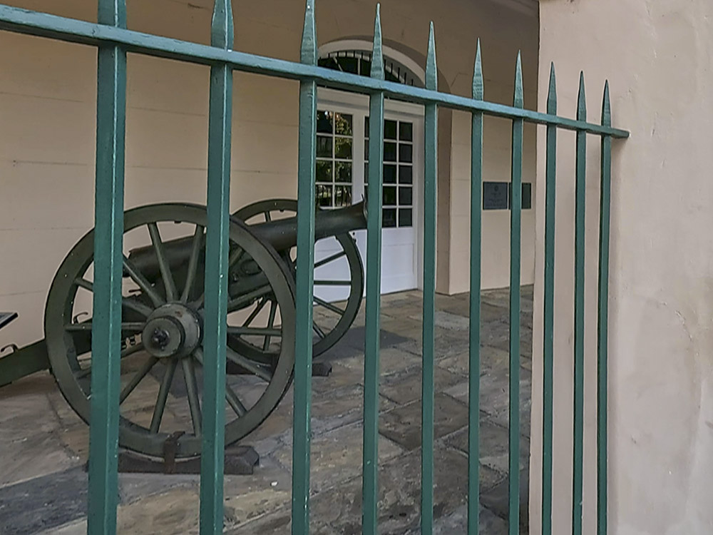 green colored iron fence in front of cannon and beige stucco building