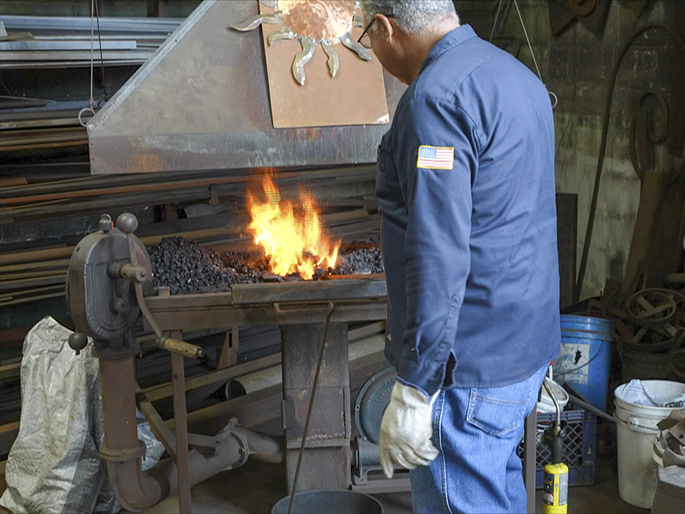 man in blue work clothes works blacksmith fire pit