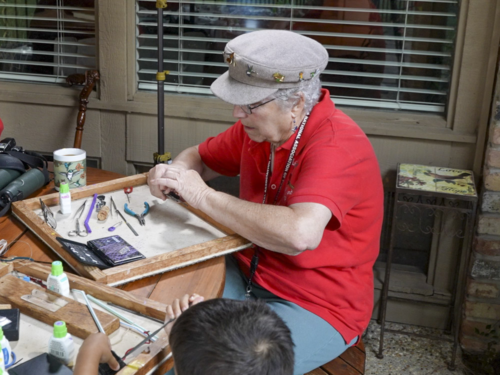 woman wearing red shirt and cap sits at table banding Louisiana hummingbirds