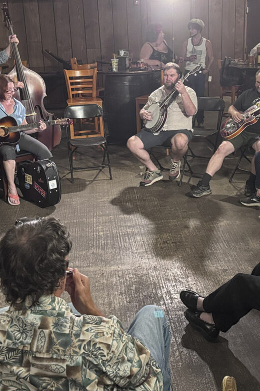 musicians with guitars banjos and fiddles sit in circle for New Orleans jam session