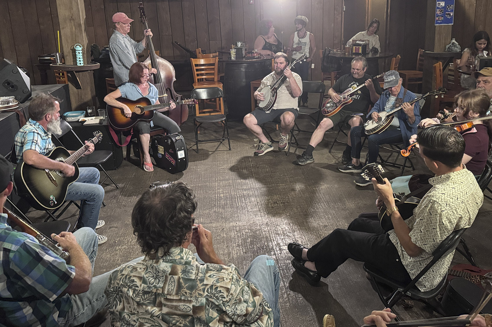 musicians with guitars banjos and fiddles sit in circle for New Orleans jam session