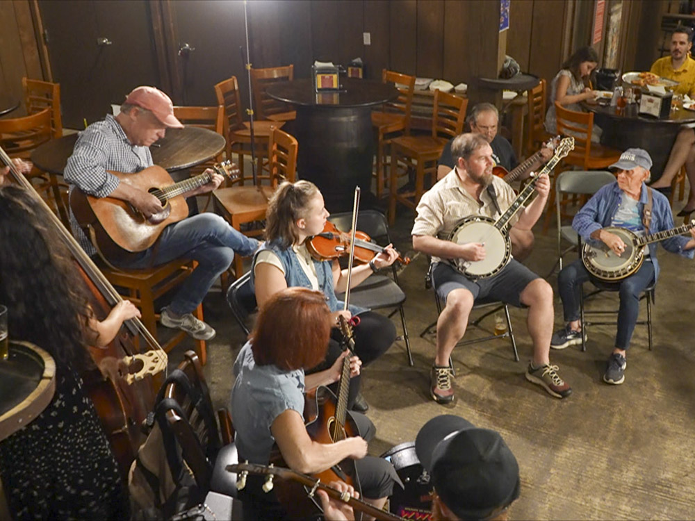 woman playing fiddle,man playing bando, others play guitar at jam session
