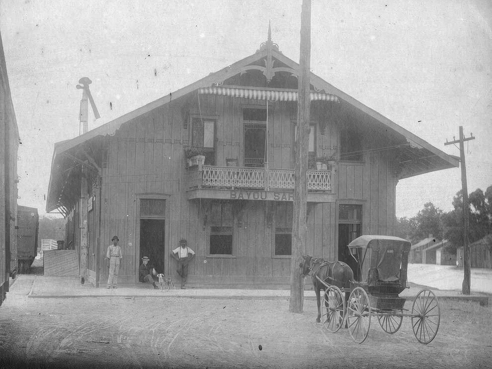 black and white image of train depot with sign Bayou Sara with people and a horse and buggy