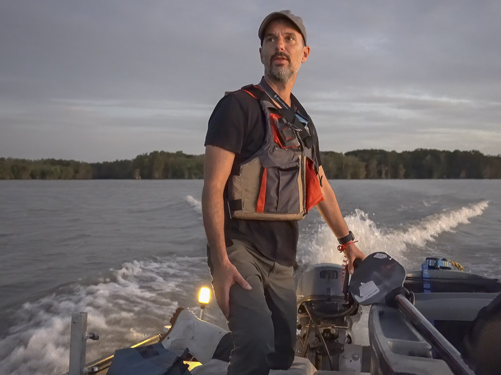 Frank Relle stands as he guides small boat through lake in the late evening.