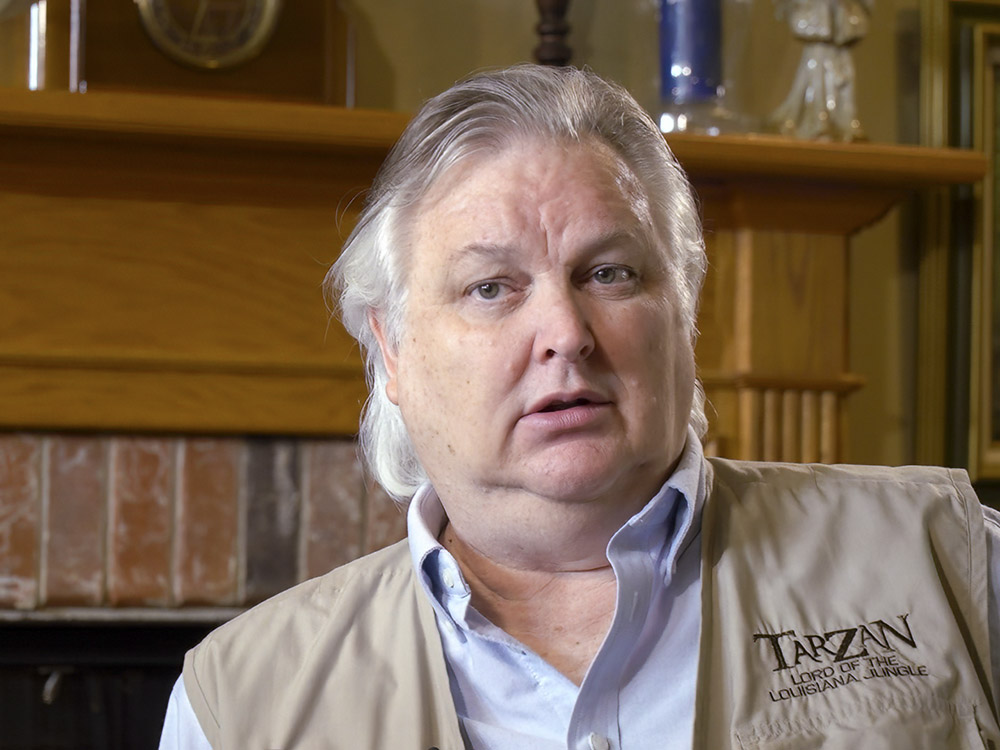 man with gray hair blue shirt and tan vest with Tarzan logo