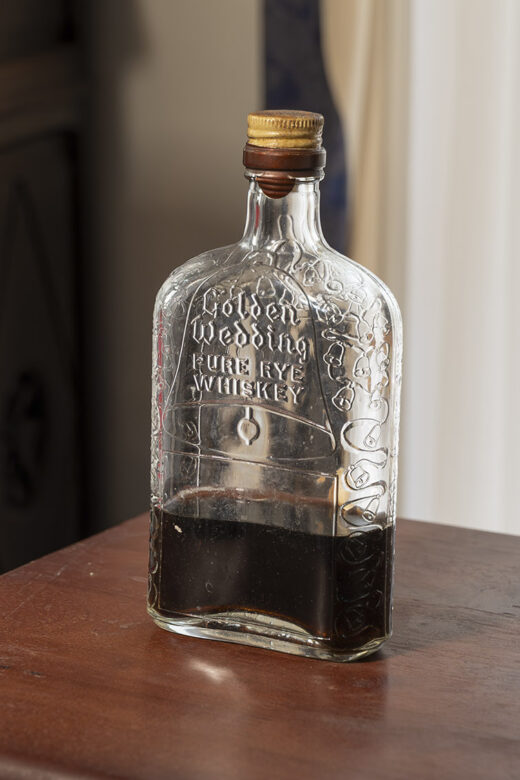 glass whiskey bottle on brown wood table with dark liquid in bottle