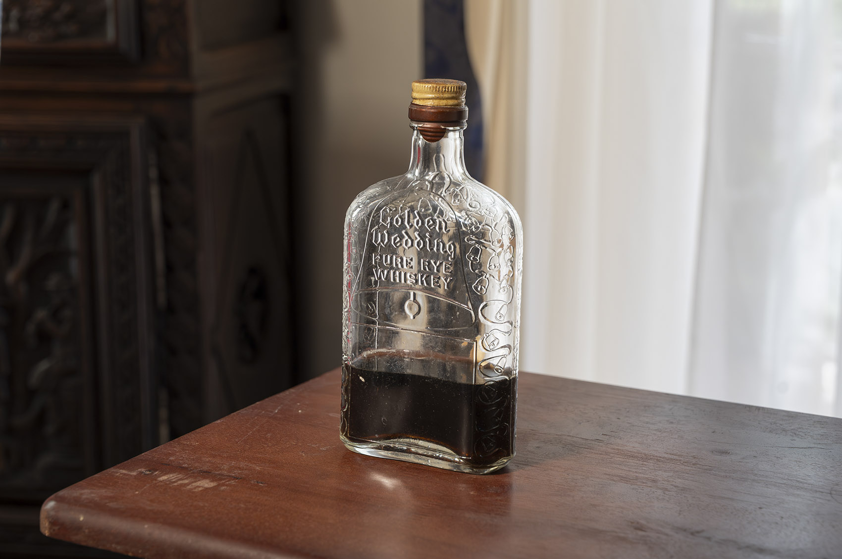 glass whiskey bottle on brown wood table with dark liquid in bottle