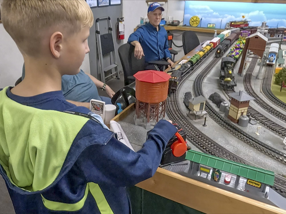 boy wit blond hair and blue and green jackets operates train set