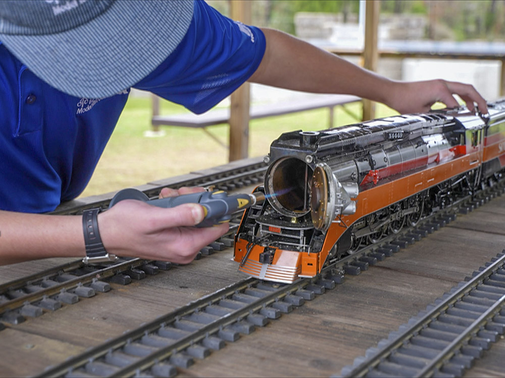 young man wearing blue shirt and cap uses butane light to start model steam locomotive
