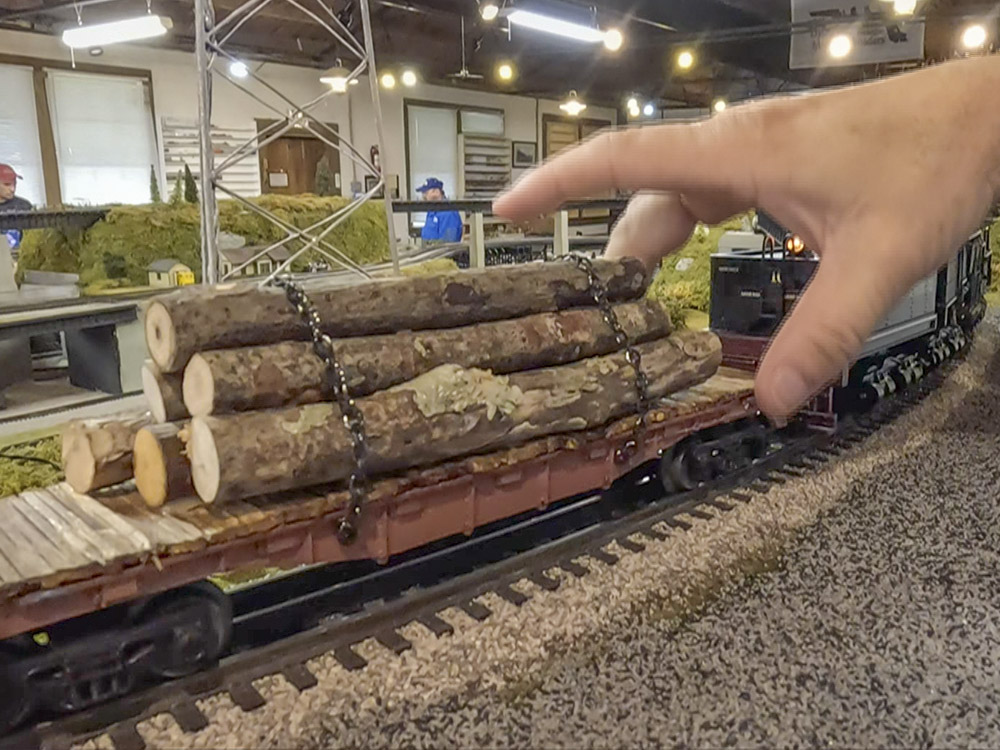 hand over miniature logs on a flat rail car on tracks in train layout