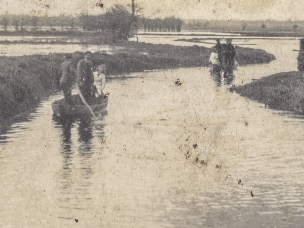 black and white photo of people in small row boats in flooded field