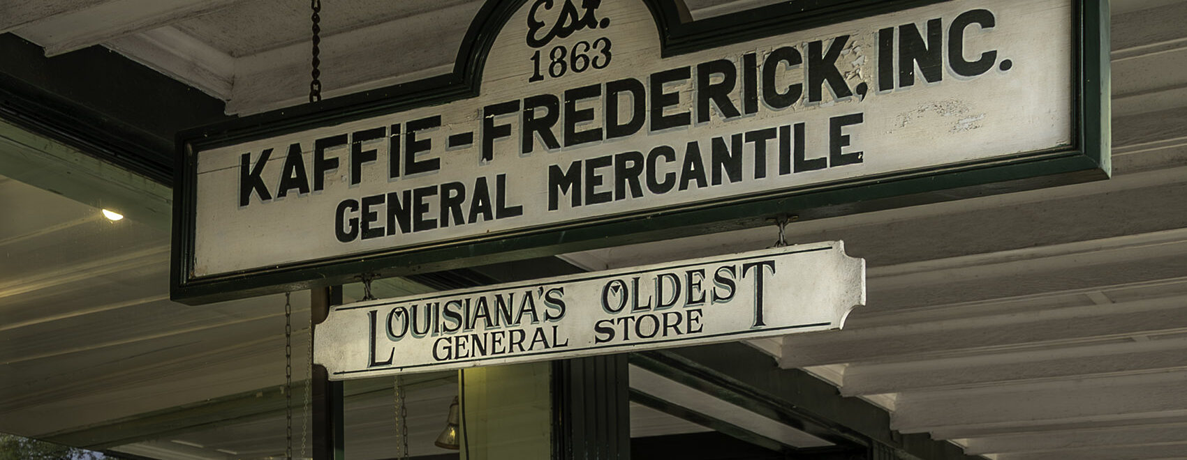 white and green sign hanging under porch for Kaffie-Frederick, Inc General Mercantile Store