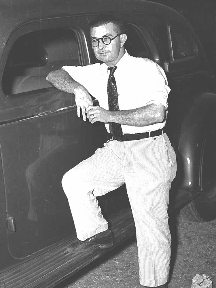 black and white photo of man wearing white shirt and tie, light colored pants and wearing black glasses
