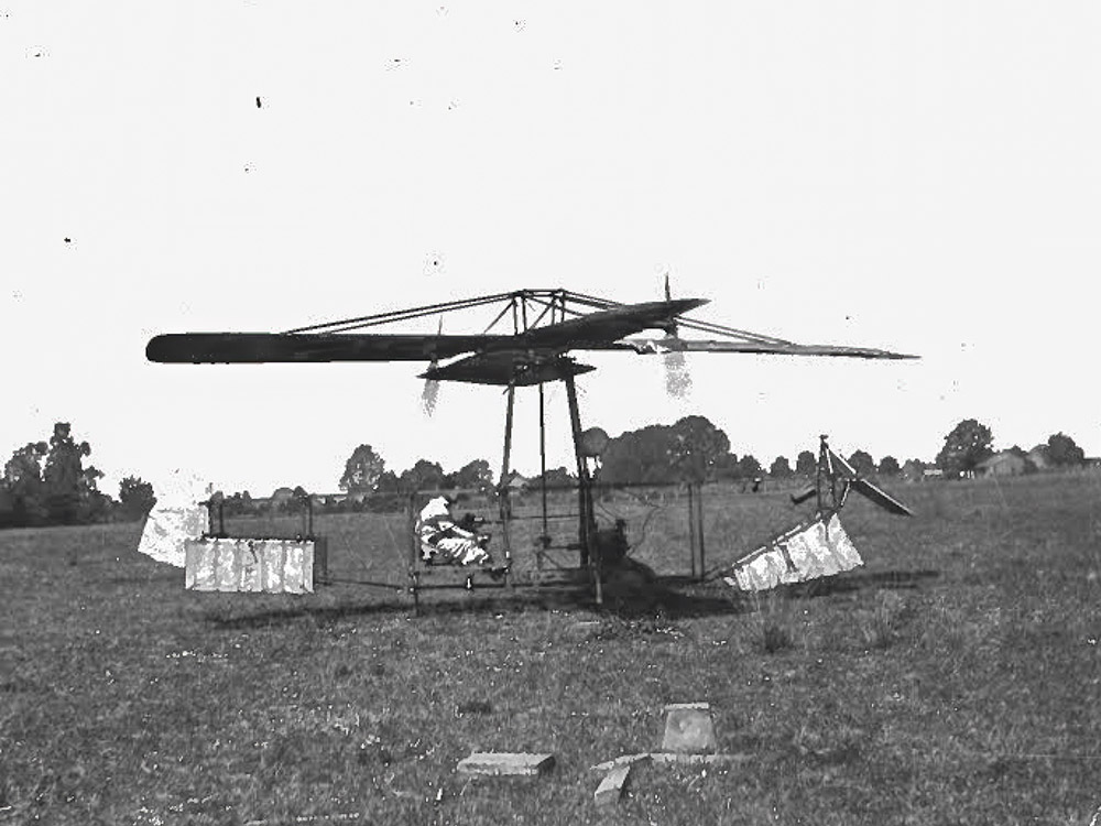 black and white photo of man sitting in an early helicopter flying machine