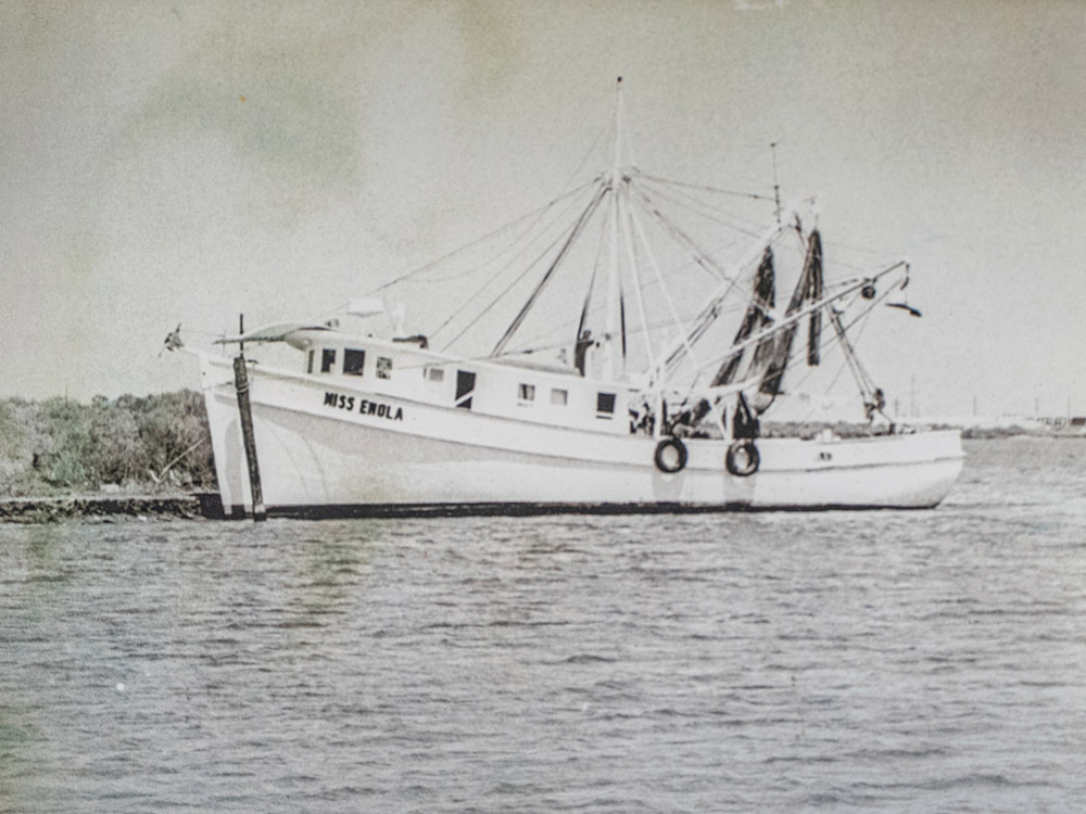 black and white photo of large shrimp trawler docked along shoreline