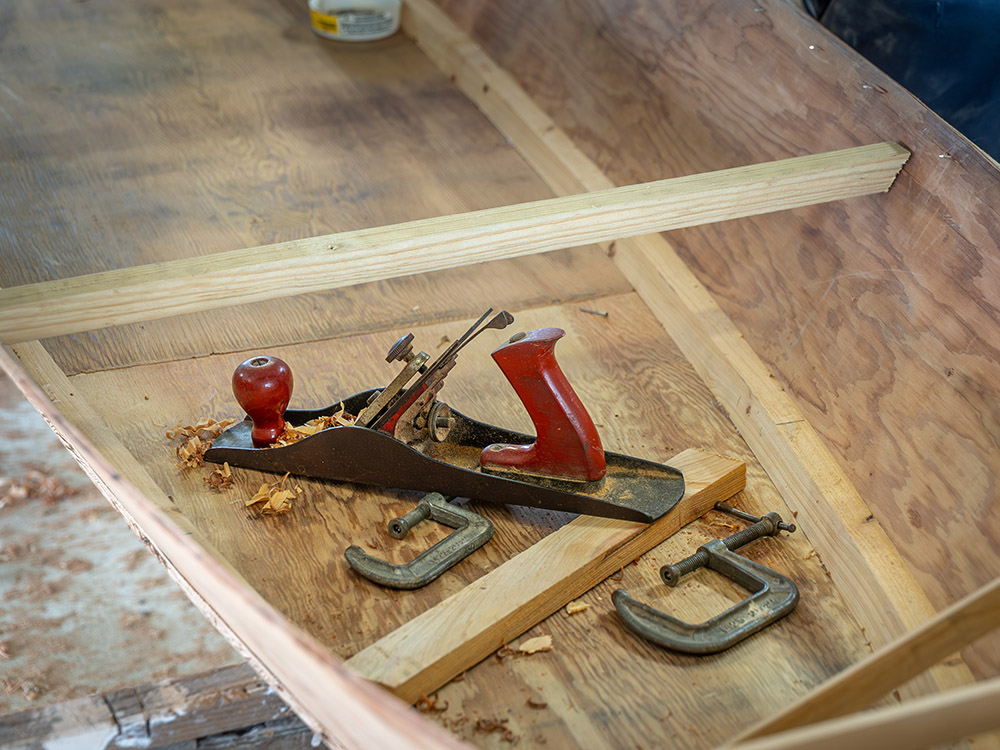 wood plane and metal clamps inside a small wood boat under construction