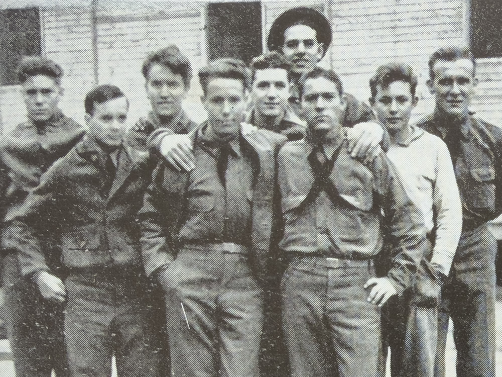 black and white photo of men in work uniforms in front of white wood building