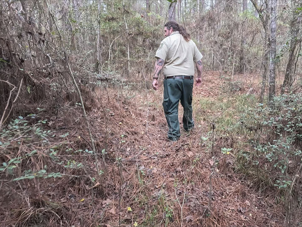 man in greet and tan uniform walks trail in forest