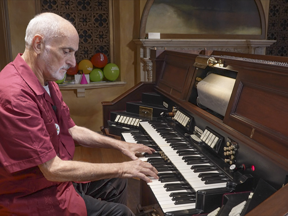 man with red shirt and gray hair plays organ