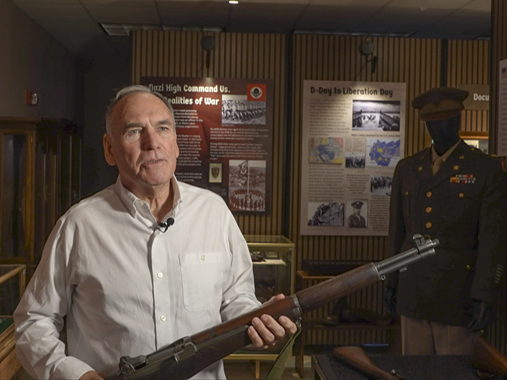 man in white shirt holding military rifle in museum