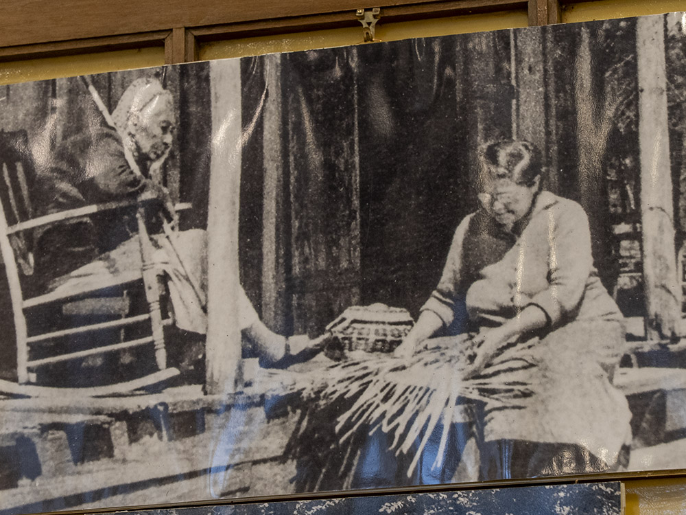 old black and white photo of two elderly women sitting on porch - one in rocker and the other weaving a basket