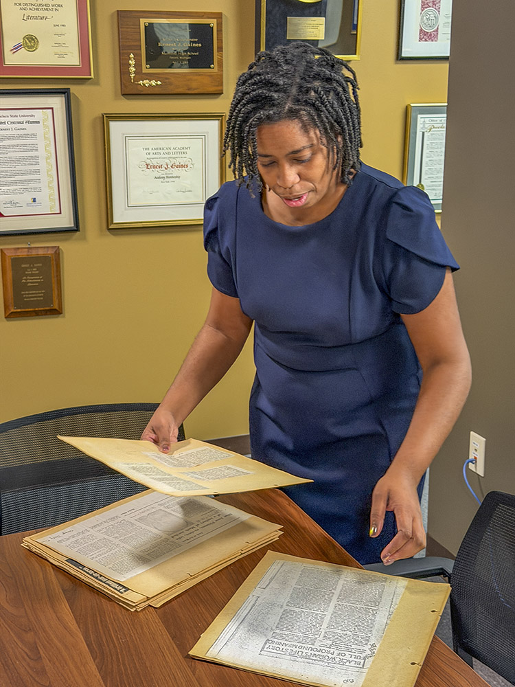 woman in dark blue dress looks at manuscriptps in file folders